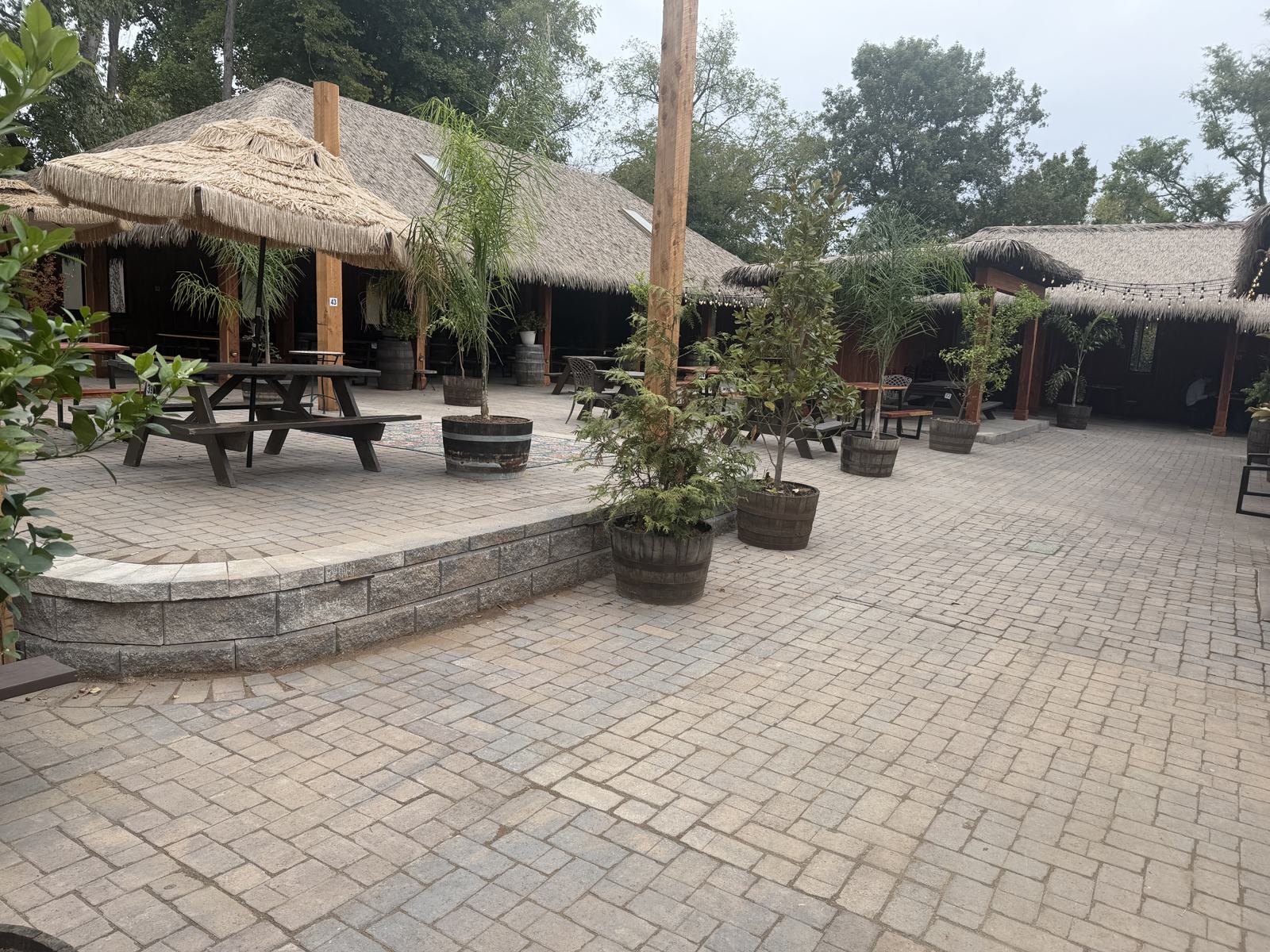 2,500 SF Belgard Aqua-Bric permeable paver courtyard at El Fuego on Gallatin Pike, Nashville, with a curved raised terrace, palm thatch roofs and barrel planters