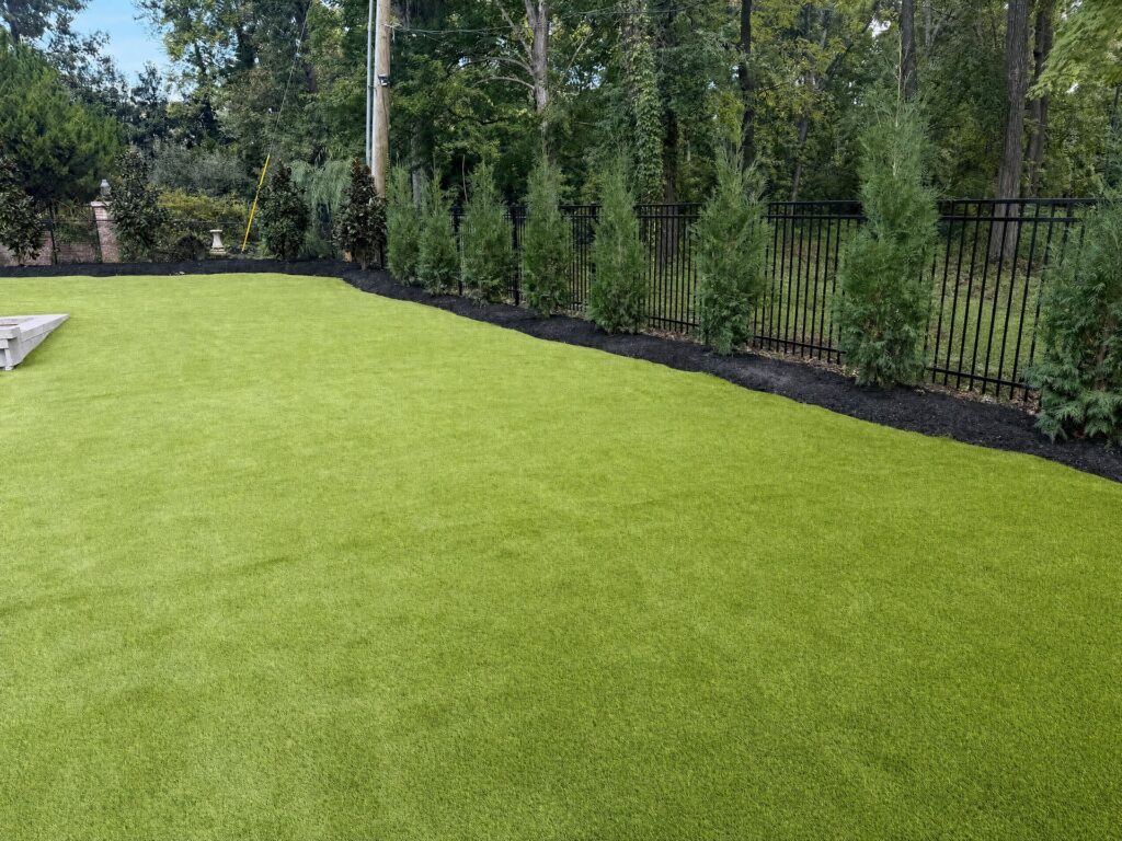Synthetic turf edged against a mulch bed of arborvitae along a black aluminum fence in Nashville
